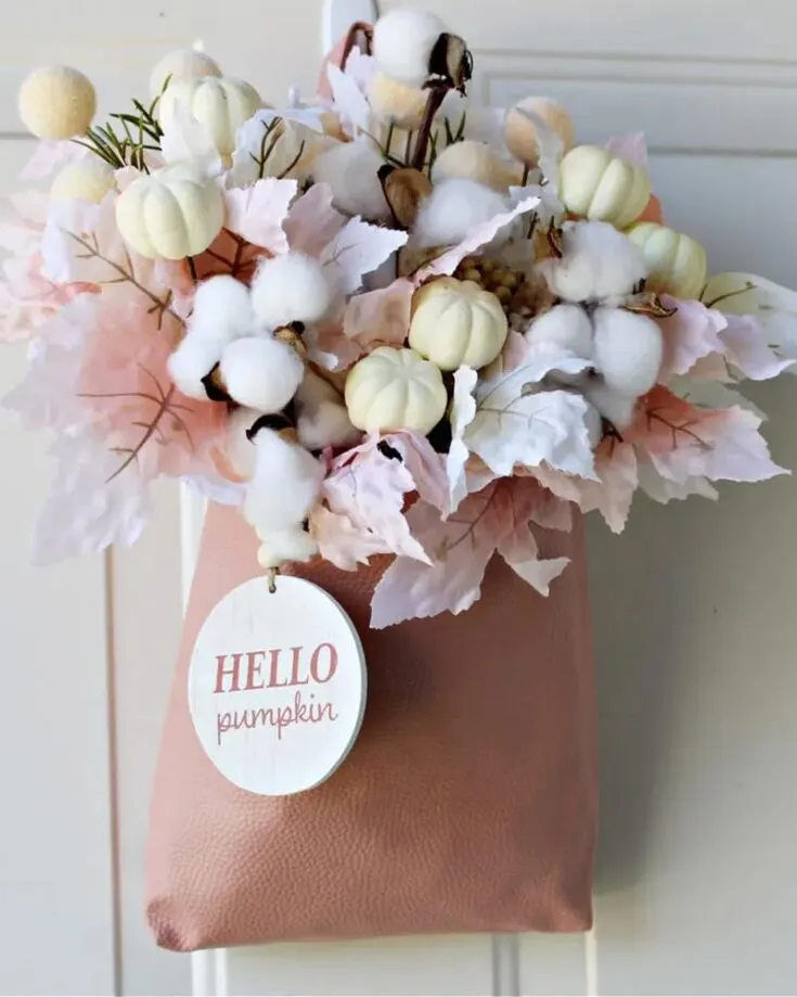 Welcome the autumn season with a fall door hanger crafted from dollar store finds of blush colored leaves and a faux leather handbag. Since no hot glue is needed for this craft, you can easily remove the fall stems and repurpose the bag to make another door sign or use it for grocery shopping!