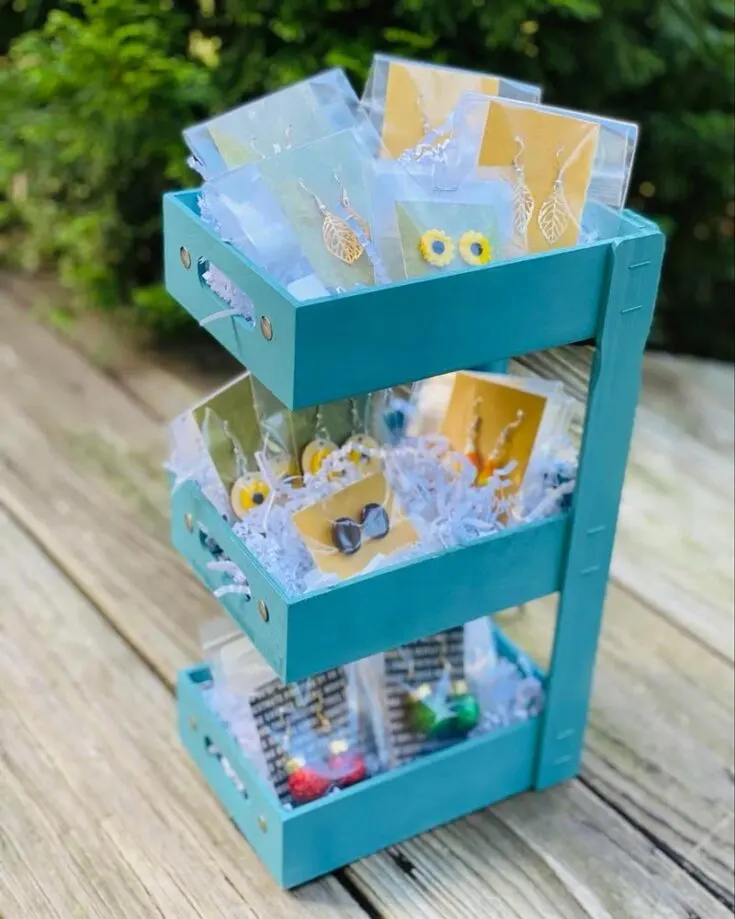 This three tiered shelf crafted from dollar store wooden trays is perfect for displaying small decor items or as an organizational tool in your kitchen, bathroom, or office to store and showcase essentials like spices, toiletries, stationery, or knick-knacks.