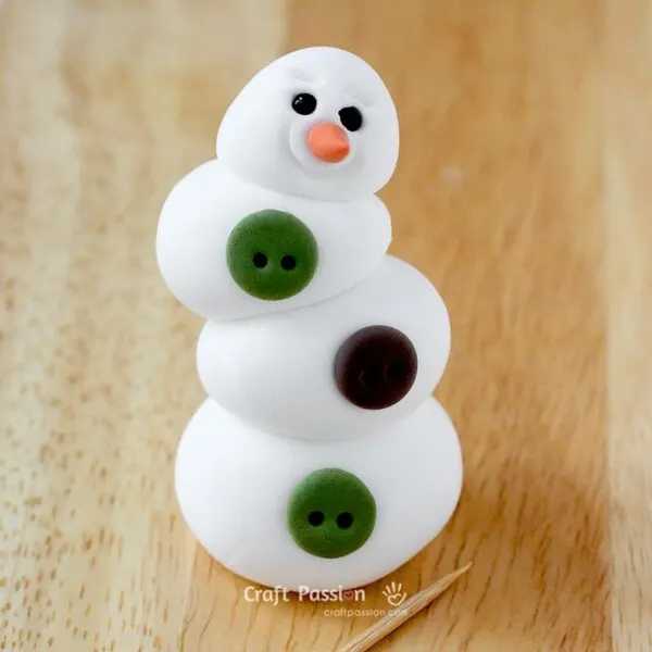 Roll two small balls from green clay and one from brown clay.

Flatten them slightly with your thumb.

Place the flattened pieces onto the snowman&rsquo;s body and poke two small holes into each to create a button-like effect.