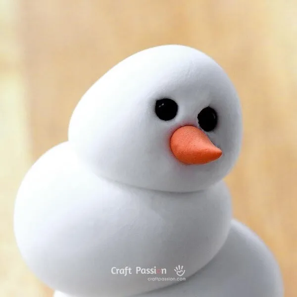 Shape a tiny piece of orange clay into an elongated teardrop for the nose.

Press the nose gently onto the face without bending its tip.
