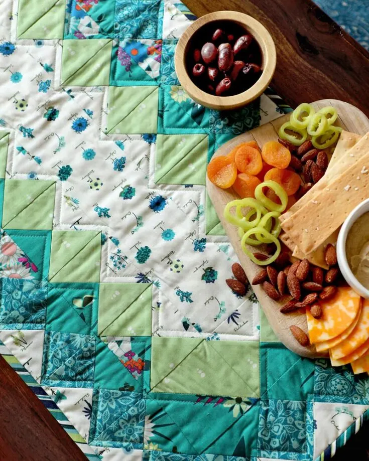 Usher in the beauty of spring with this beautiful table runner pattern. It's an intermediate quilting project that features lovely floral prints with geometric HSTs of blue and vibrant pinks with subtle greens. This Mediterranean design adds a breath of fresh air to your home decor.&nbsp; Table runner size: 15" x 36"