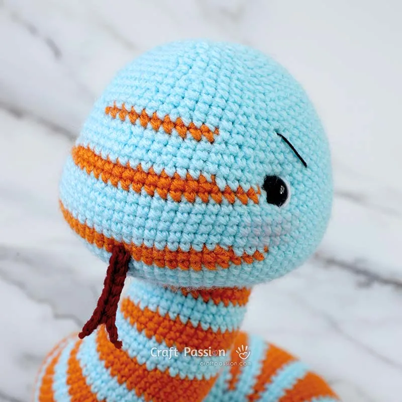 Sew brows, attach a forked tongue, highlight the eyes with white yarn, and lightly brush on blusher to give Suki, your crochet snake, an irresistibly cute face that's full of charm and personality!
