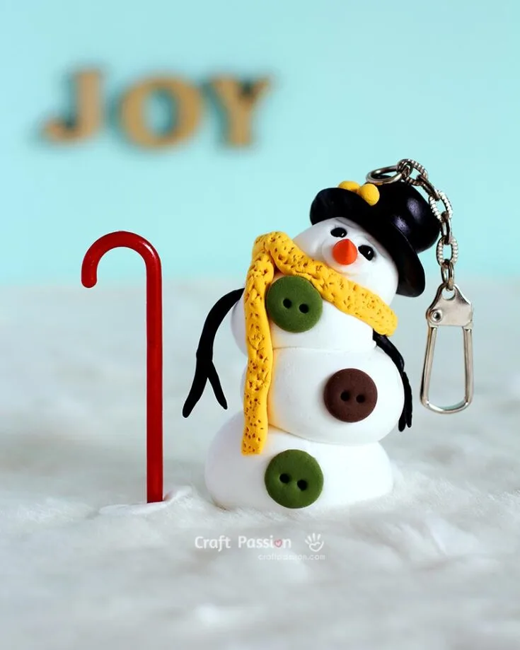 DIY a mini snowman ornament from air-dried lightweight clay for a touch of winter fun! With a yellow scarf, button details, and a black hat, it&rsquo;s a cute, customizable keychain or holiday decoration.