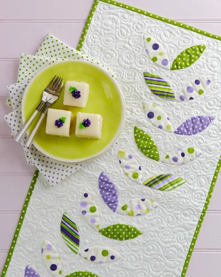 Take a look at this beauty! It's the go-to design if you prefer something minimalistic for your accent piece, and it adds a pop of green to your decor. It features appliques with extra pop using batting and freezer paper for a trapunto effect.&nbsp; Table runner size: 16" x 60"&nbsp;