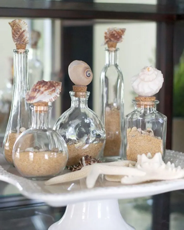 Small bottles from the dollar store make a perfect base for crafting charming decorative seashell bottles! Fill them with sand and tiny shells for a lovely touch. Add a few larger shells to the corks with hot glue, and enjoy your very own beautiful beach-themed decor!