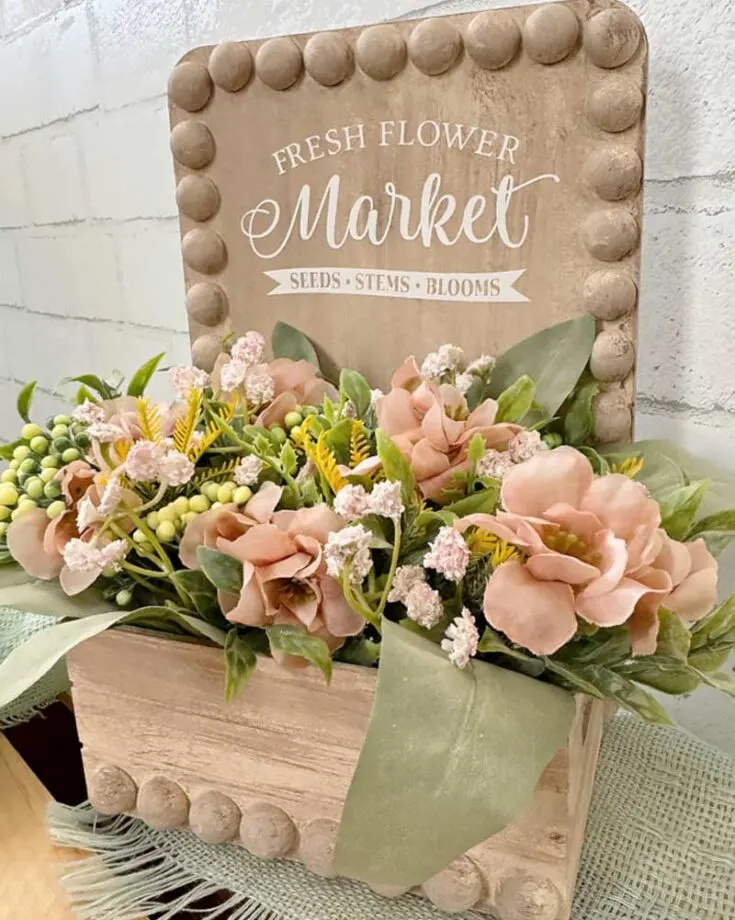 Welcome the arrival of spring into your home with this DIY flower crate crafted from dollar store supplies including a bamboo cutting board, a wood crate, and some faux greenery and flowers. This simple craft makes for a charming and colorful centerpiece for your home.