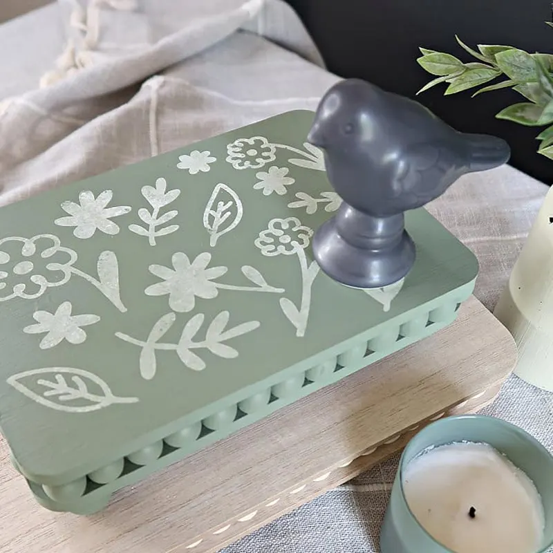Check out this stylish wood bead riser that you can craft using two wooden cutting boards and some wooden beads from the dollar store. This wood bead riser can be a versatile decor piece that elevates your living room, whether it&rsquo;s for displaying candles, plants, or other decorative items.